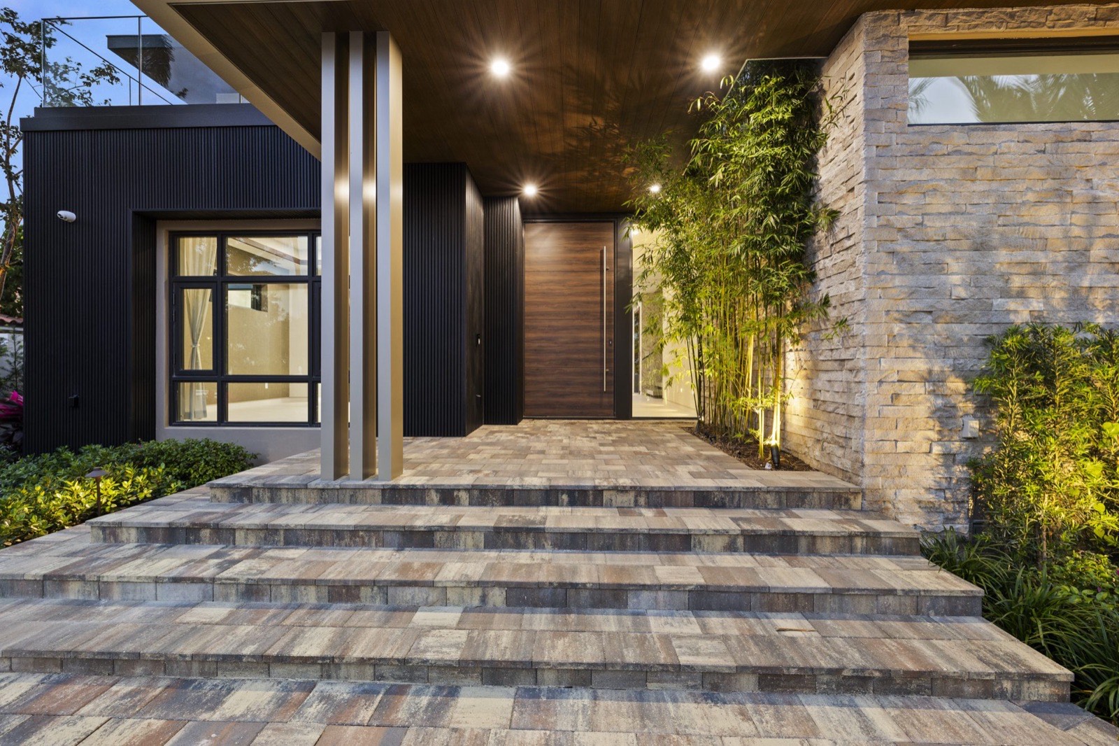 Paver entry steps, walnut front door, and stacked-stone wall under a wood-clad canopy